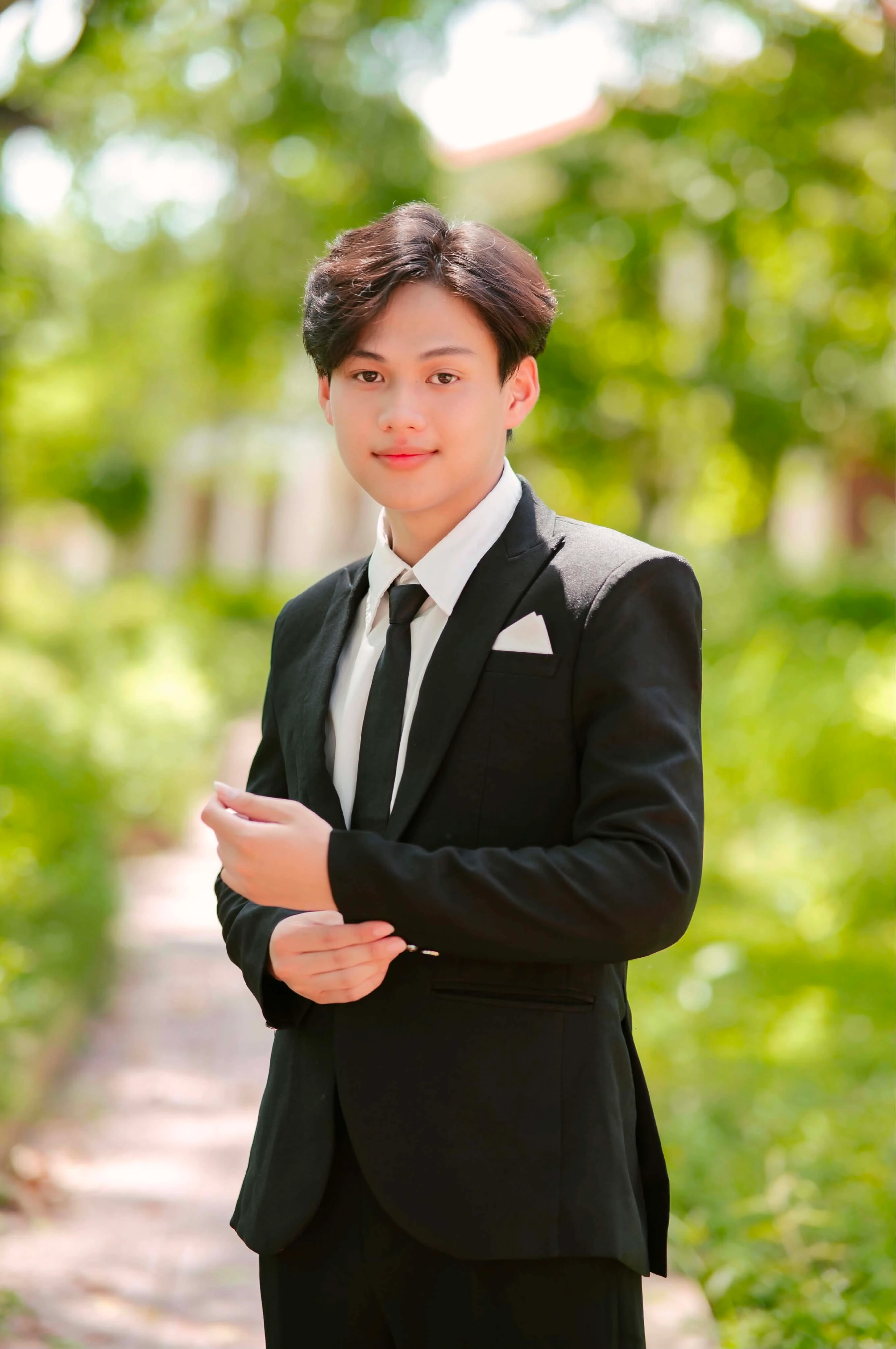 Quang in a black suit on a sunlit garden path